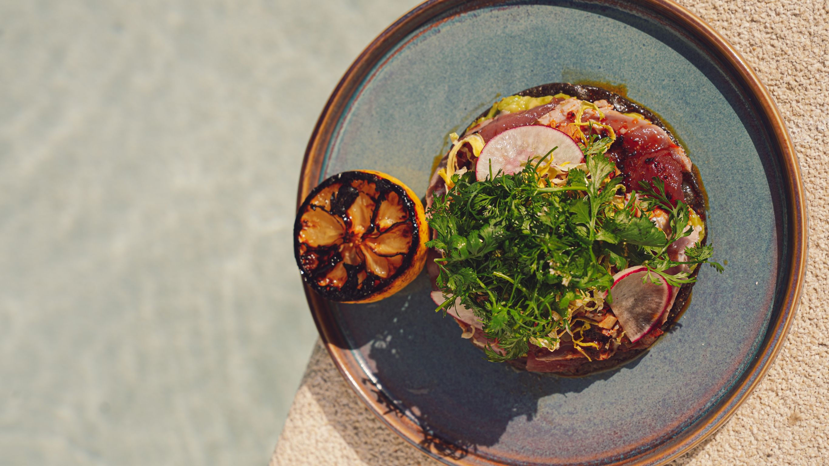 meat tacos topped with avocado on long black plate next to cactus